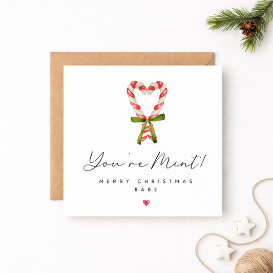You're Mint! Merry Christmas Babe card featuring a watercolour candy cane heart tied with a green ribbon bow, with a pink heart, sent with a kraft envelope